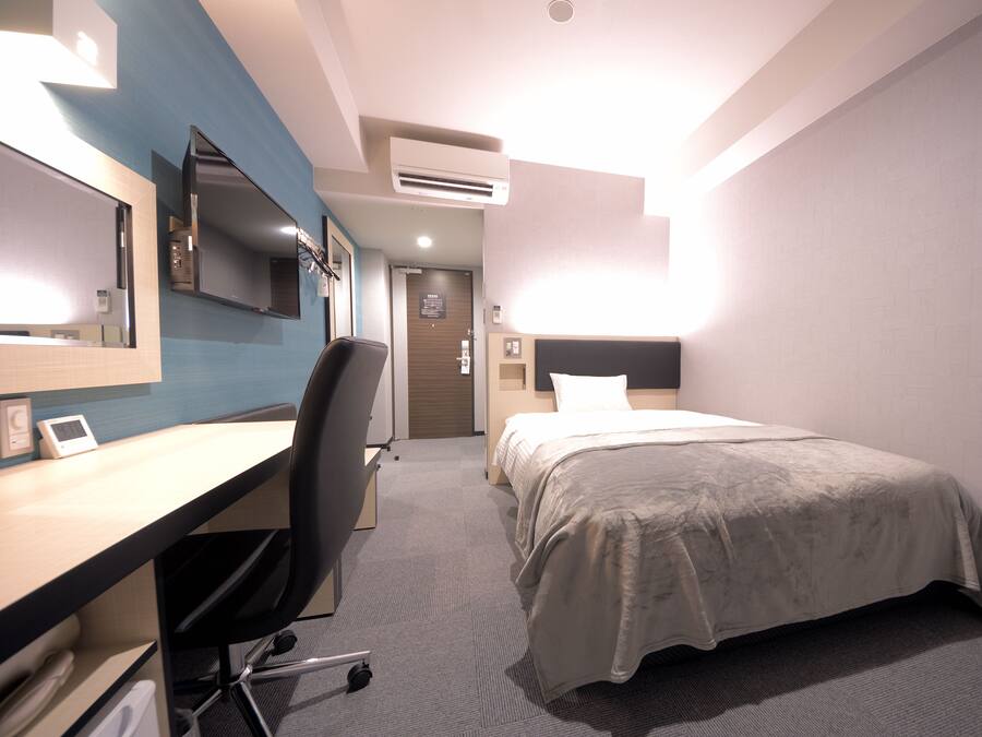 A hotel room with a desk, chair, bed, and a mirror.