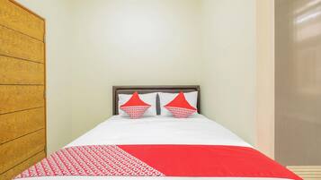 A single bed with a white and red bedspread, two red pillows, and a wooden wardrobe to the left.