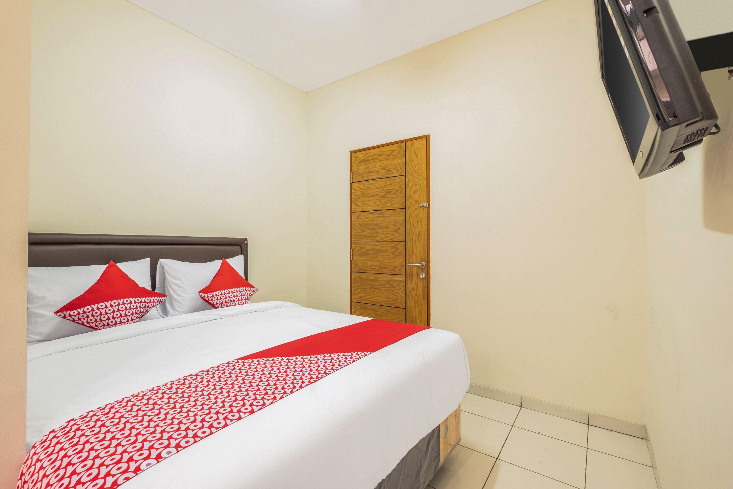 Une chambre d’hôtel avec un lit, une porte en bois et un téléviseur fixé au mur.