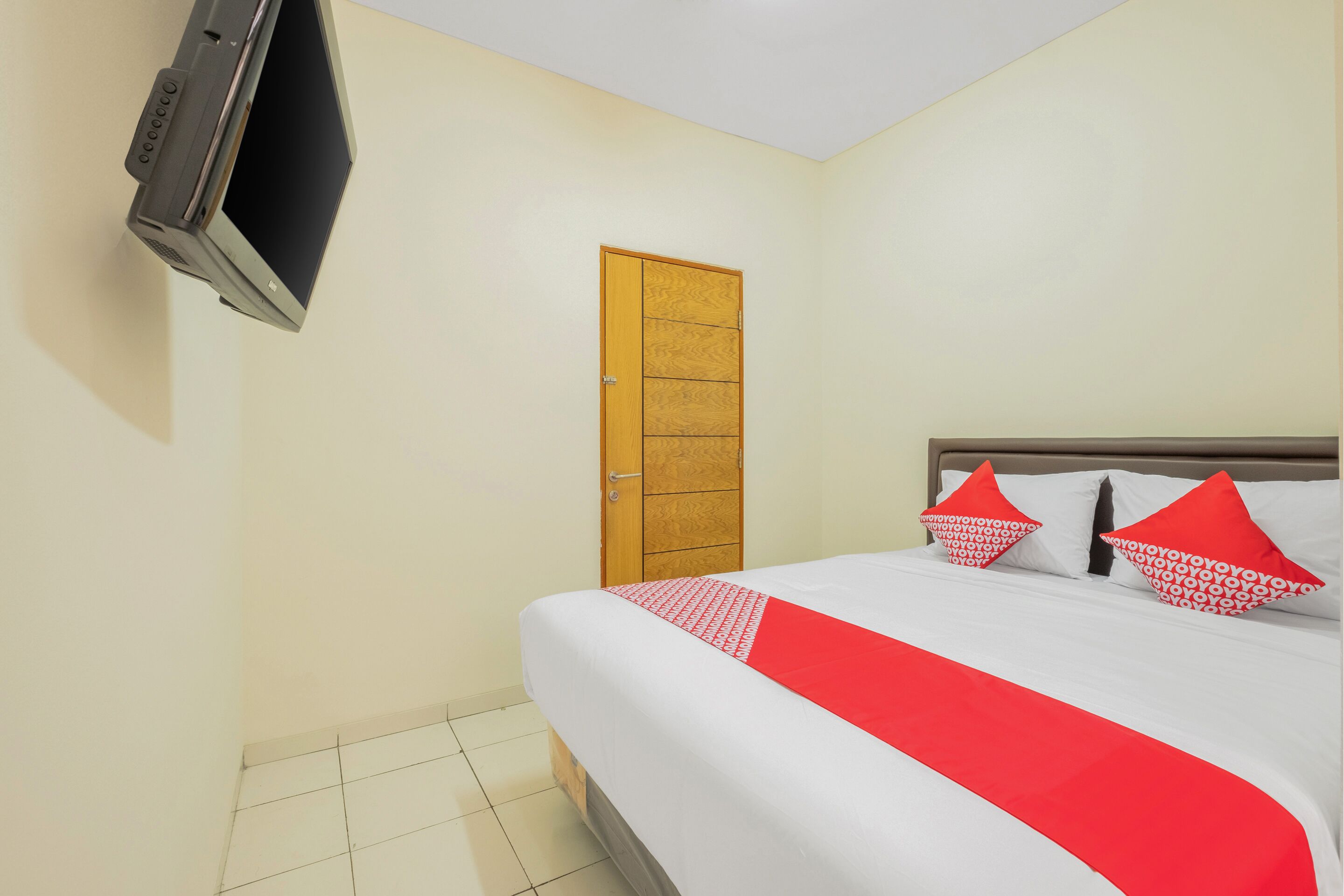 Una habitación de hotel con una cama, un televisor en la pared y una puerta de madera.