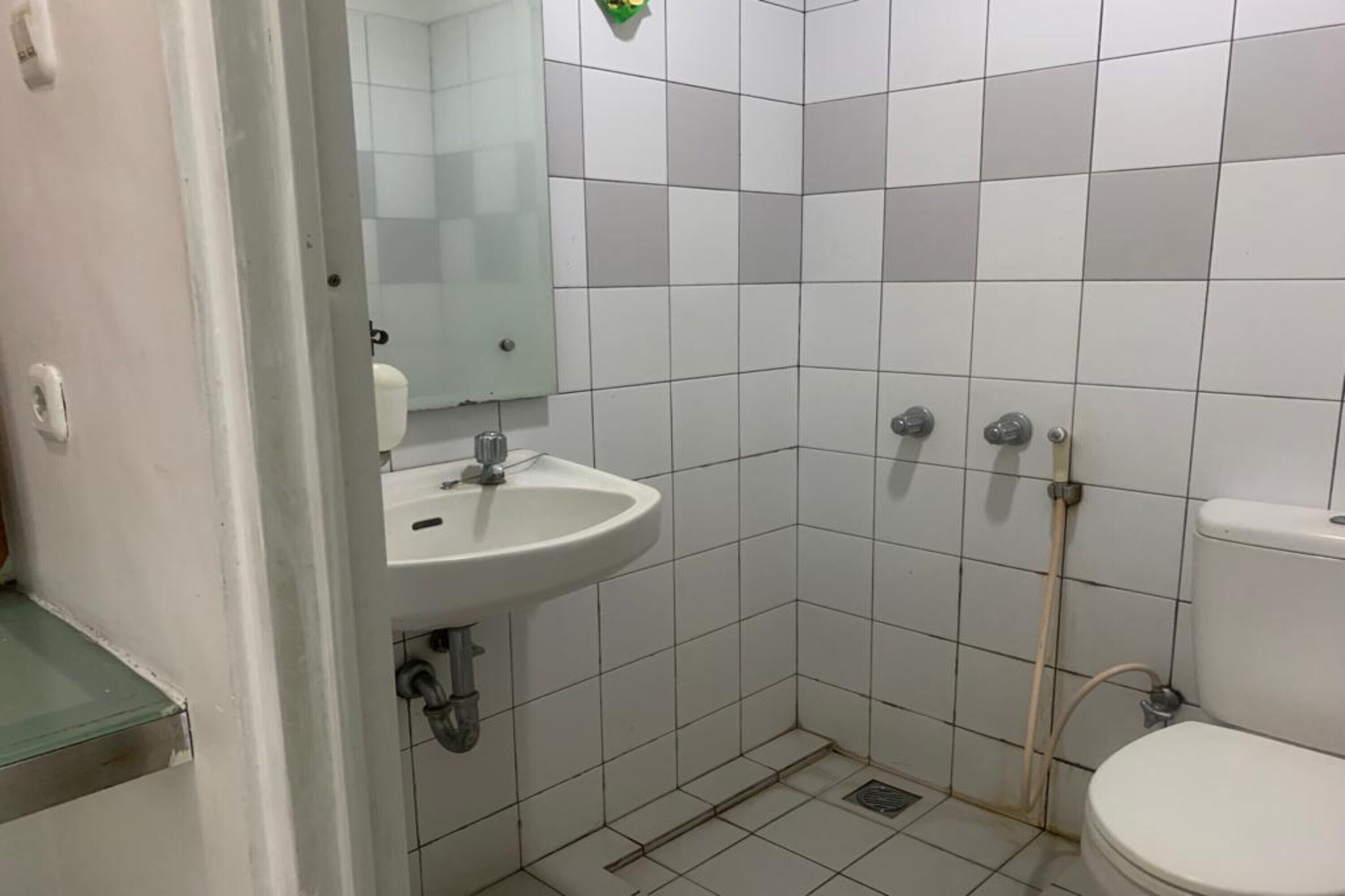 A small, tiled bathroom with a sink, mirror, toilet, and shower.