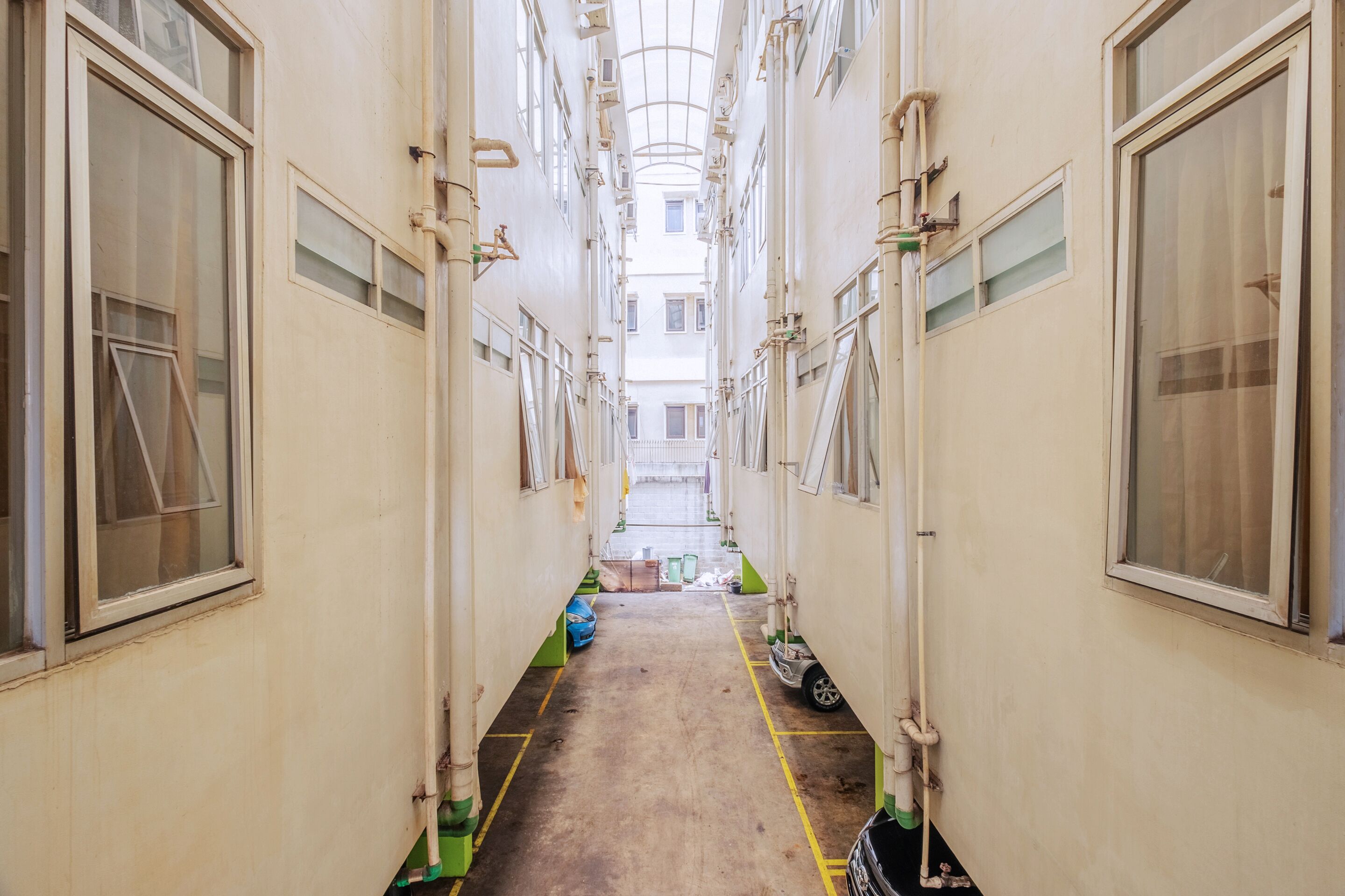 Un pasillo estrecho con techo alto, varias ventanas y tuberías a la vista.