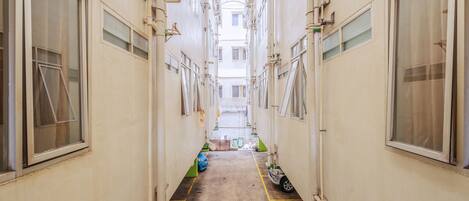 Un pasillo estrecho con techo alto, varias ventanas y tuberías a la vista.