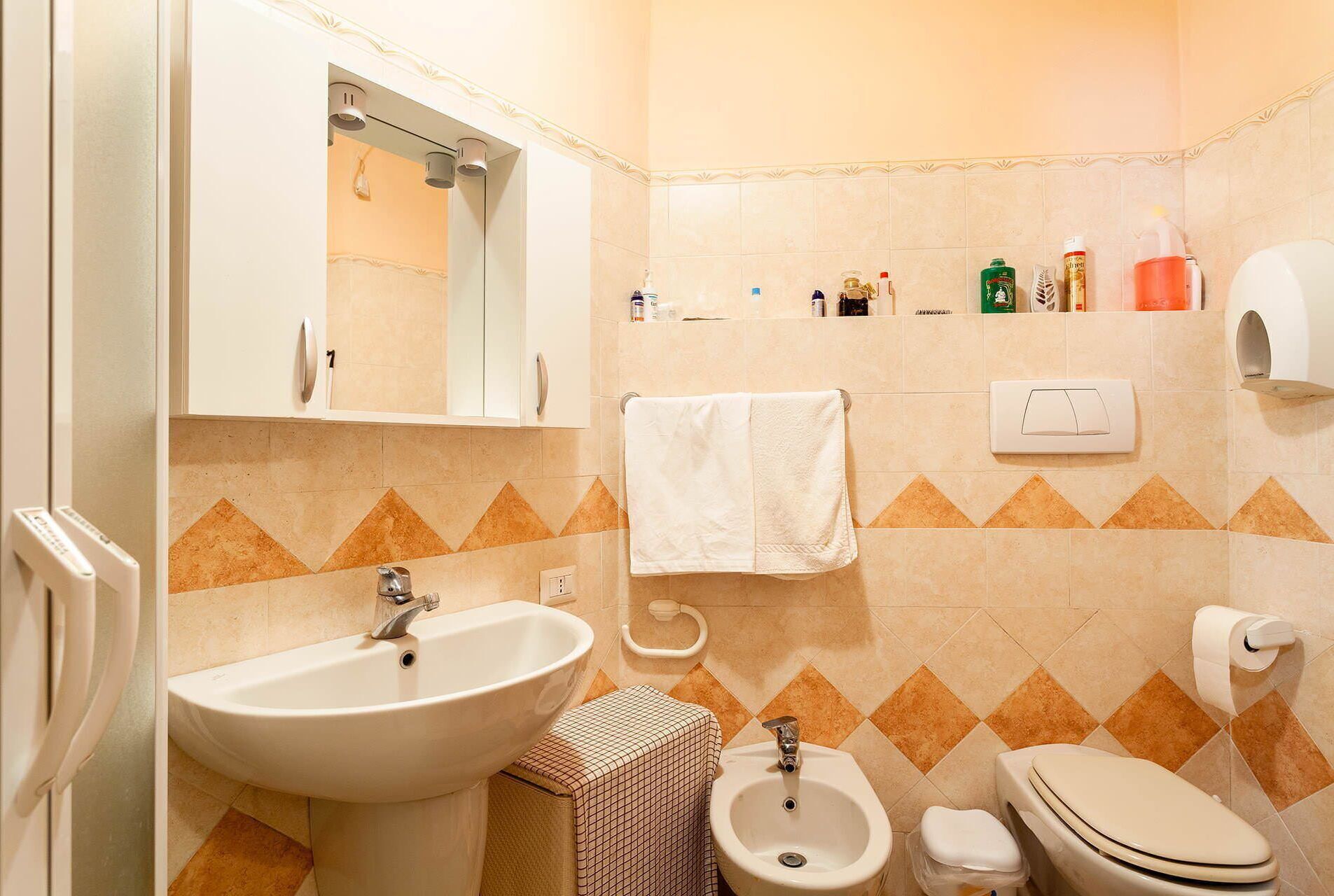 Een badkamer met een wastafel, spiegel, handdoekrek, toilet, bidet en toiletartikelen aan de muur.