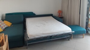 Habitació amb un llit, un sofà, una taula petita amb una làmpada, un aparell d'aire condicionat i una finestra amb cortines.