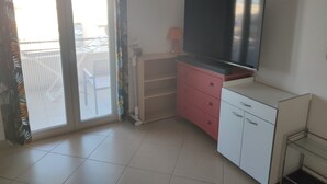 Habitació amb porta corredissa de vidre que dona a un balcó, televisió de pantalla plana penjada a la paret, un taulell de nit rosa i un armari blanc.