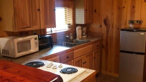 A wooden cabin-style kitchen with a stove, microwave, sink, and refrigerator. - Cabin at Sunset Ranch with Sunset Resort on Medina Lake access! (Mico)