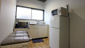 A compact kitchen with a microwave, refrigerator, sink, and a window above the counter. - The Neighbors Tsukamoto (Osaka)