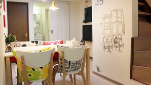 A dining area with a table and chairs, a wall with a cafe illustration, and a staircase. - The Neighbors Tsukamoto (Osaka)