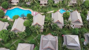 Vista aérea de un complejo turístico con varias edificaciones tipo bungalow, una piscina central y abundante vegetación.