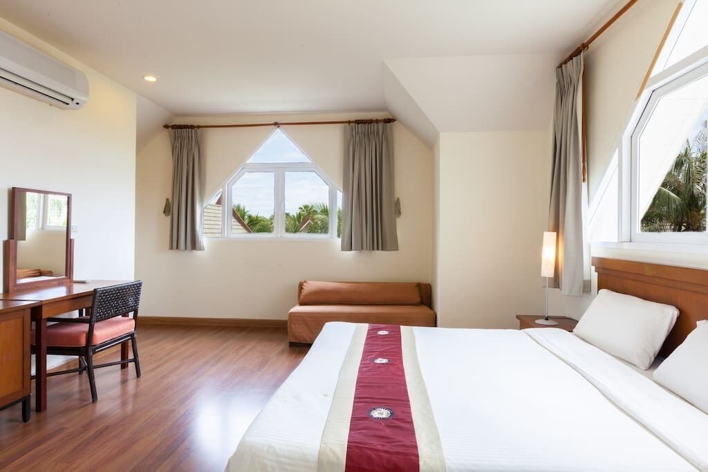 Een hotelkamer met een bed, een bureau, een stoel, een raam met gordijnen en uitzicht op groen.