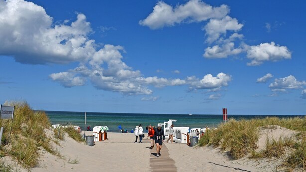 Une plage avec une promenade en bois menant à la mer, un panneau indiquant « Terrilstrand », et un panneau rouge et blanc visible au loin.