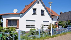 Une maison blanche avec un toit rouge, une antenne parabolique et une clôture bleue.