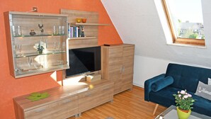 Un salon moderne avec un téléviseur, des meubles en bois, un canapé bleu et une fenêtre donnant sur des immeubles.