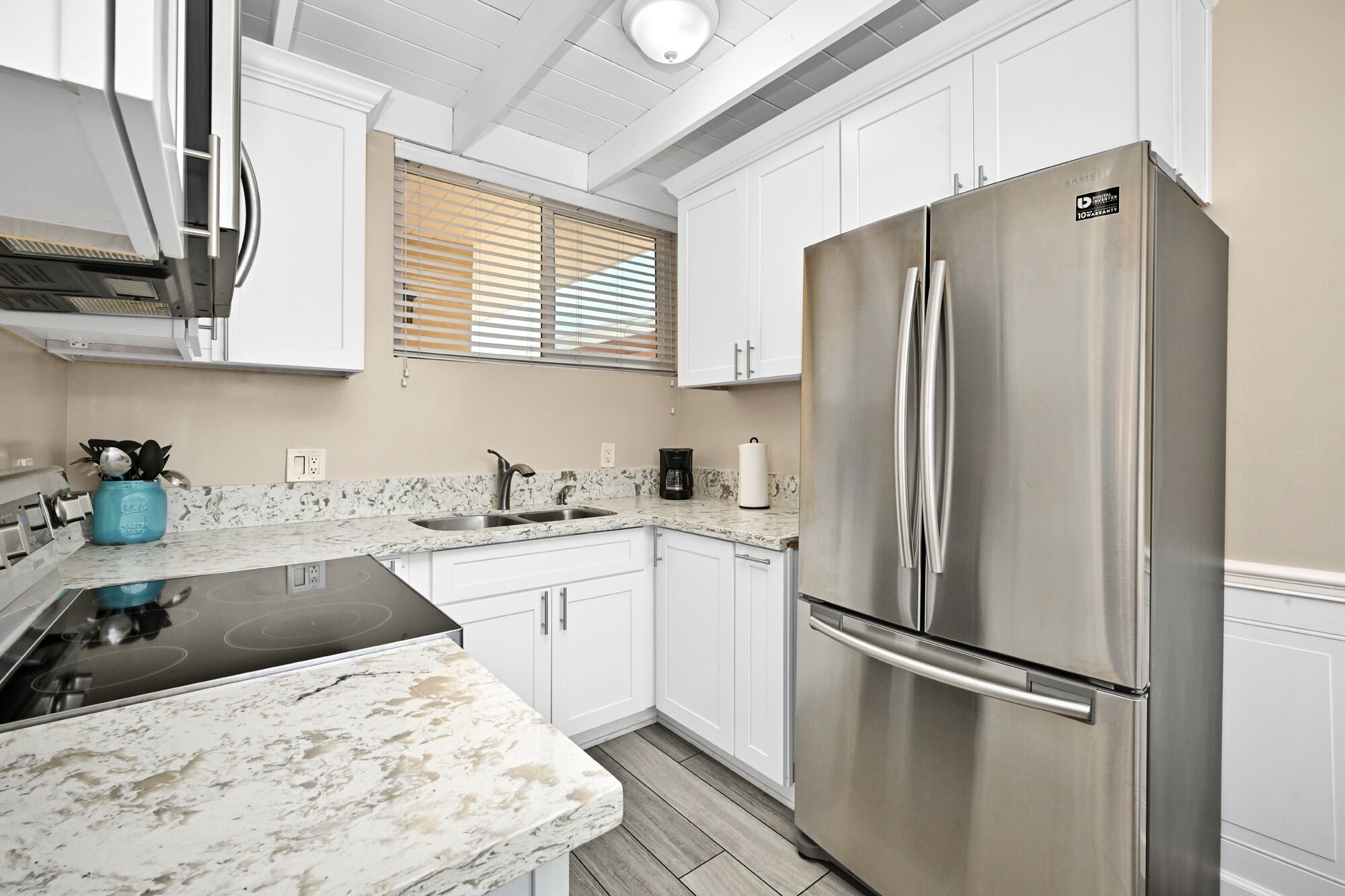A modern kitchen with white cabinets, a stainless steel refrigerator, a black stovetop, and a marble countertop.