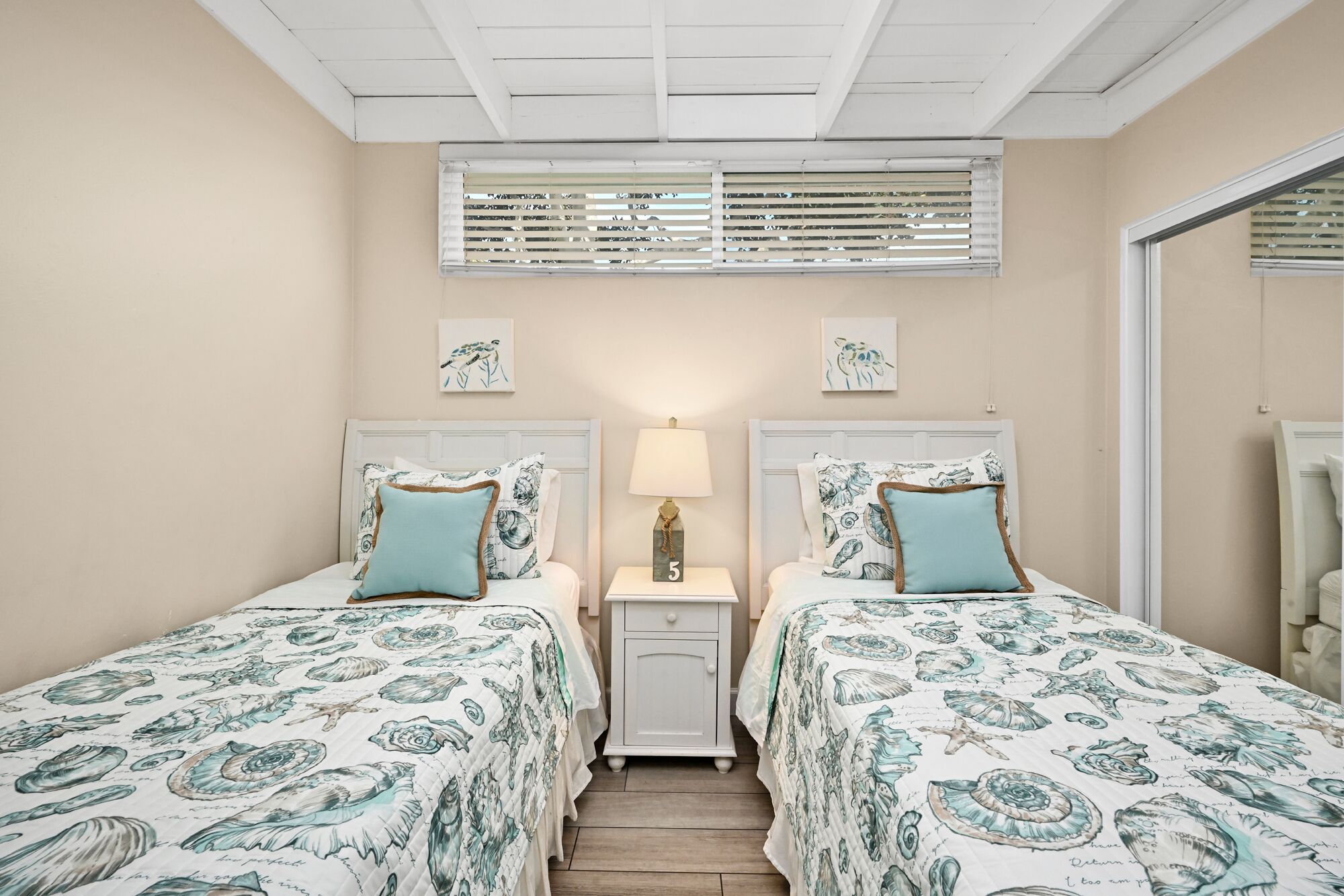 Een slaapkamer met twee bedden, elk voorzien van een bloemenbedekking, een nachtkastje met lamp en kunstwerken aan de muur.