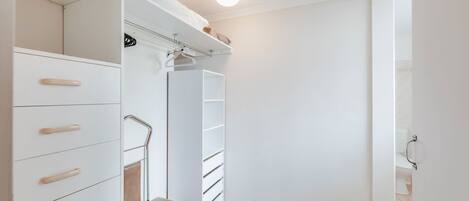 A walk-in closet with white storage units, a bench, and a hanging rack.