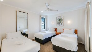 A hotel room with two beds, a ceiling fan, a large mirror, a window with curtains, and a wall-mounted light. - Horizons 3-16 Miller Bargara (BARGARA)