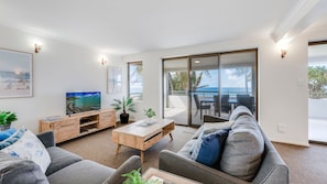 A modern living room with a flat-screen TV, a wooden coffee table, grey sofas, and a balcony with a view of the sea. - Horizons 3-16 Miller Bargara (BARGARA)