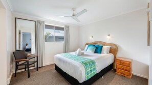 Habitación de hotel con una cama, una silla, una mesita de noche de madera, un ventilador de techo y una ventana.