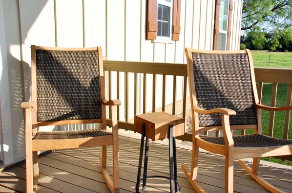 Deux fauteuils à bascule sur une terrasse en bois, avec un mur blanc et une fenêtre en arrière-plan.