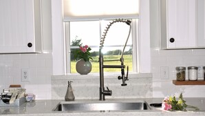 Una cocina con un lavamanos de acero inoxidable, un jarrón con flores y una ventana que da a un campo.