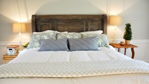 Una cama bien hecha con una colcha estampada, dos almohadas y un cabecero de madera. Hay dos mesitas de noche con lámparas y una pequeña planta en maceta.