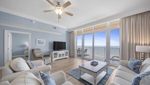 A spacious living room with a ceiling fan, a flat-screen TV, and a large window offering a view of the ocean. - Direct Beachfront Lazy River Waterslide-Hot tub-Indoor Pool-Walk to restaurants (Orange Beach)
