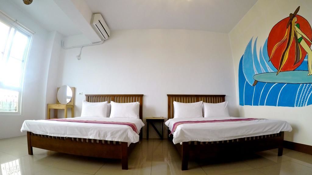 A hotel room with two wooden beds, white bedding, a small round table, a wall-mounted air conditioner, and a mural of a sailboat.