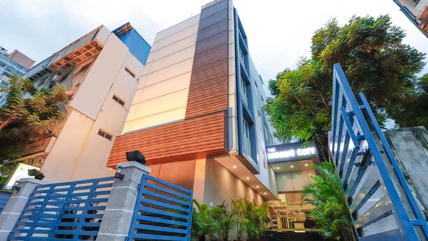Entrada de hotel moderna com um letreiro chamativo, um portão azul e vasos de plantas.