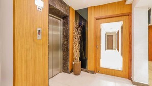 Um saguão de hotel com parede de madeira, elevador de mármore e porta com espelho.
