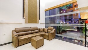 Uma sala de estar moderna com um sofá seccional de couro marrom e um banquinho, uma janela grande com vista para o exterior e um luminário fixado na parede.