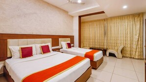 Quarto de hotel com duas camas, cabeceira de madeira, uma janela grande com cortinas, uma mesinha e uma cadeira.