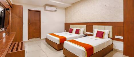 A hotel room with two beds, a wooden desk, an air conditioning unit, and a ceiling fan.