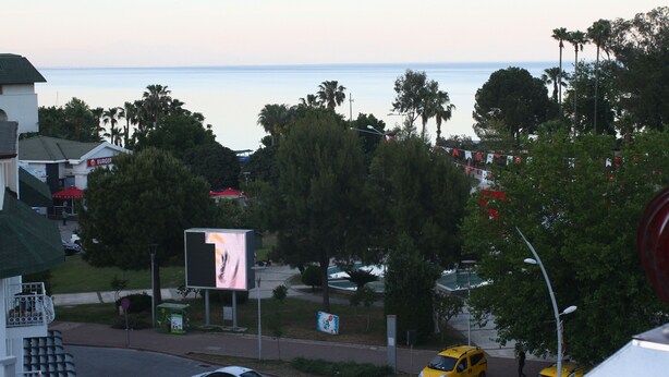 A coastal view with a road, palm trees, and a billboard. - Liman Boutique Otel (Kemer)