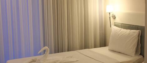 Habitación de hotel con dos camas, cada una con una colcha blanca y una toalla. Hay una lámpara de pared a la derecha de la cama.