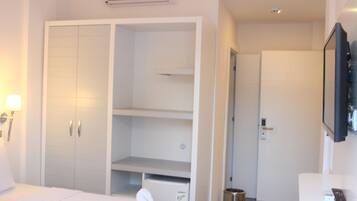 A hotel room with a large wardrobe, a bedside table, a TV mounted on the wall, and a door leading to another room.