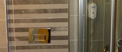 A modern bathroom with a striped tile wall, a glass shower enclosure, and a toilet with a flush handle.