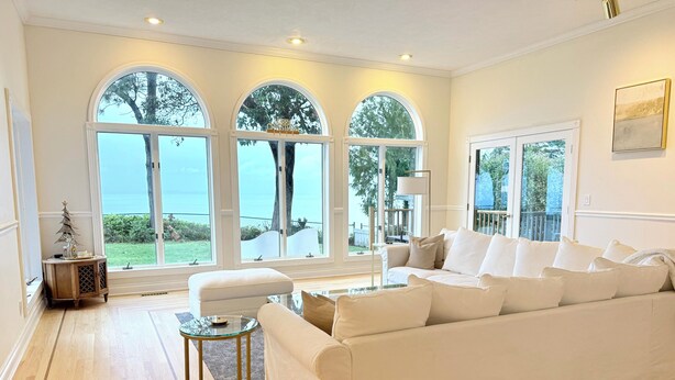 Un salón espacioso con un sofá blanco grande, una mesa de centro de cristal y suelo de madera. Hay tres grandes ventanales que ofrecen vistas al exterior.