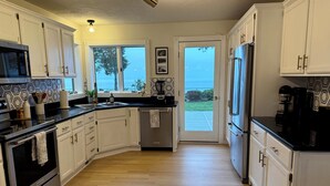 Una cocina moderna con armarios blancos, electrodomésticos de acero inoxidable y vistas al exterior a través de un ventanal.