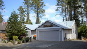 Een huis met twee verdiepingen, met een garage, omgeven door hoge bomen en een houten hek.