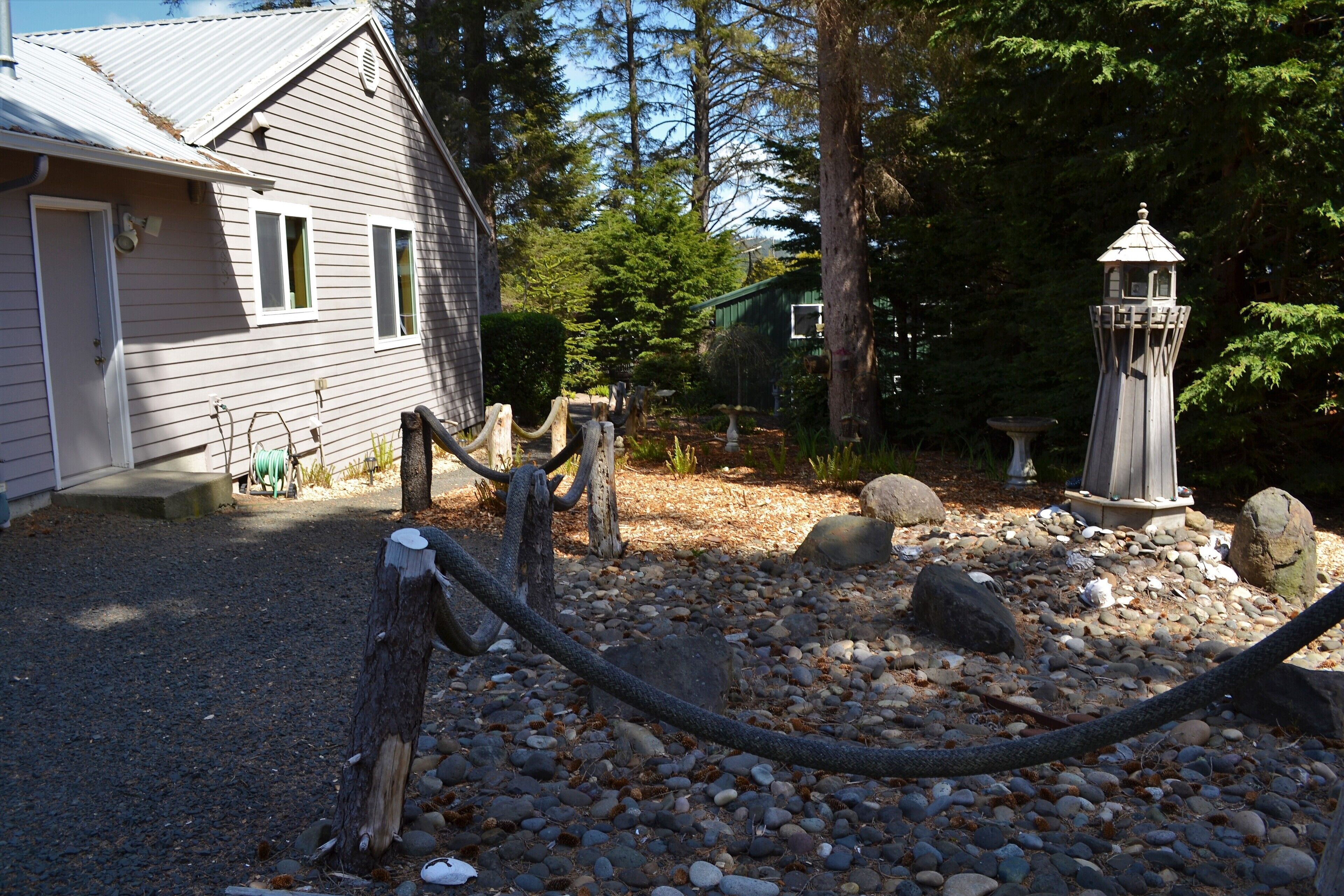 A rustic wooden house with a gravel driveway, surrounded by trees and a decorative lantern.