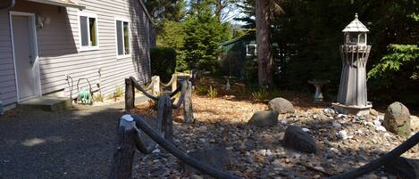 A rustic wooden house with a gravel driveway, surrounded by trees and a decorative lantern.