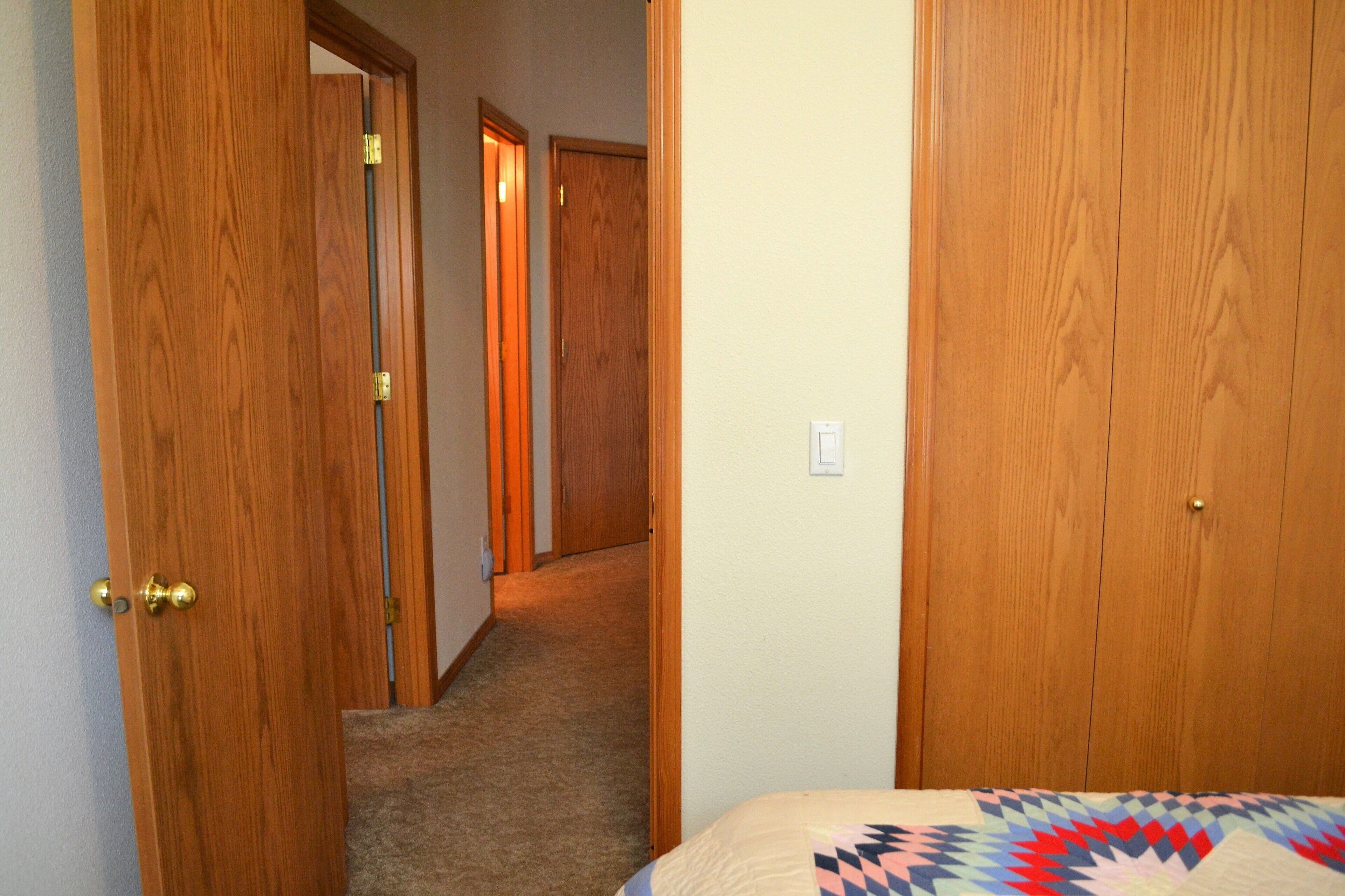A hallway with wooden doors, carpeted floor, and a bed with a patterned bedspread.