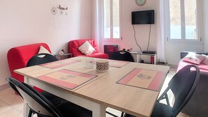 Una habitación con una mesa de madera, sillas rojas y negras, un televisor en la pared y una ventana con cortina.