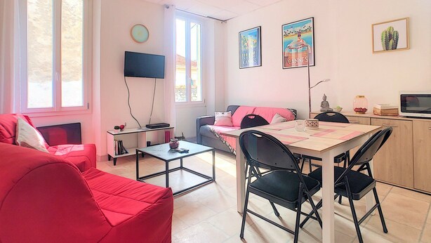 Una sala de estar moderna con un sofá rojo, una mesa de comedor con sillas, un televisor de pantalla plana montado en la pared y obras de arte en las paredes.