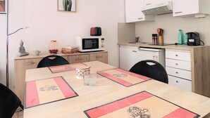 Una cocina compacta con microondas, tostadora y cafetera sobre la encimera. Hay una mesa de comedor con manteles individuales y sillas.