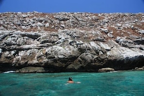 A rocky coastal area with clear turquoise water and a person swimming.