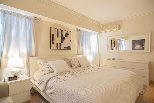 Une chambre à coucher bien rangée, avec un lit, des tables de chevet, une horloge numérique et des œuvres d’art accrochées aux murs.