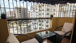 Ein Balkon mit Korbmöbeln, einem Glastisch und Blick auf Gebäude durch ein Metallgeländer.